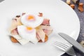 Benedict eggs with bacon and ham. Served on a white plate with a fork and knife on gray background. Royalty Free Stock Photo