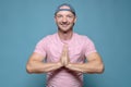 Benevolent, smiling man folded hands in a namaste gesture. Blue background.