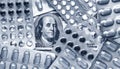 Benjamin Franklin`s head with dollar bills looks among blisters with classic blue pills, medicine flat lay