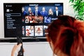 Redhead woman sitting in her living room and holding a television remote control facing a