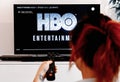 Woman watching television watching a series produced by HBO which we see the logo at the
