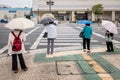 Four women with umbrellas stand in front of a pedestrian crossing