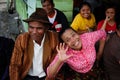 Very cheerful laughing and fumbling Indonesian elderly woman in a pink blouse and her stylishly dressed man in a brown hat