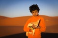 Berber child holding a desert fox poses in the Erg Chebbi dunes in Morocco.