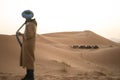 Berber man watching a group of dromedary camels in the dunes of the Sahara desert