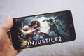 Berdyansk, Ukraine - March 4, 2019: Hands holding a smartphone with Injustice 2 game on display screen