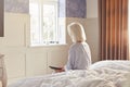 Bereaved Senior Woman Sitting On Edge Of Bed Looking At Photo In Frame