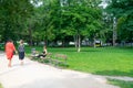 Woman sits crossed legged reading in exercise clothing on park bench while two women walk past holding hands