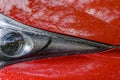 Headlight of a car with metallic red car paint with raindrops