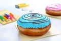 Berliner donut with blue frosting on a white office desk and materials for creativity. Snack dessert at the workplace, lunch break