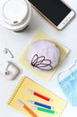 Berliner donut, coffee, headphones, medical mask and materials for creativity on a white office desk. Snack dessert at the