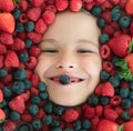 Berries child face close up. Top view photo of child face with berri. Berry set near kids face. Cute little boy eats