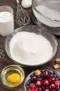 Berries, sifted flour in black plate, cocoa powder. Measuring cup with flour, glass of milk, broken egg and salt, metal whisk