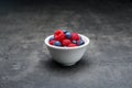 Berry fruit in white ceramic bowl on dark concrete background.