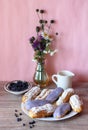 Berry glazed eclairs with blueberries on a wooden background with a decor consisting of a vase with wildflowers and a Royalty Free Stock Photo