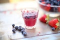 berry juice in clear cup, dewy berries scattered nearby