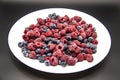 A Berry mix  from frozen raspberries and blueberries on the white plate. A Frozen Berries in black background.  A sweet background Royalty Free Stock Photo