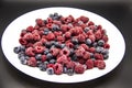 A Berry mix  from frozen raspberries and blueberries on the white plate. A Frozen Berries in black background.  A sweet background Royalty Free Stock Photo