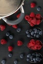 Berry raspberries and blueberries, lies in four spoons on a black background, in the corner there is a cooking vessel