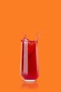 Berry red fresh juice in glass with reflection, bright colorful splashes, flying drops and swirl on orange background, copy space Royalty Free Stock Photo