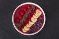 Berry smoothie bowl with chia seeds, bananas, blueberries, currant and raspberries on black slate background