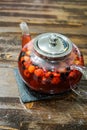 Berry tea in a glass teapot on a wooden table.