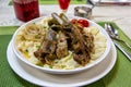 Beshbarmak dish: noodles with lamb and onion close-up on a plate on the table. Large pieces of stewed meat are cooked on plates