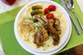 Beshbarmak dish: noodles with lamb and onion close-up on a plate on the table. Large pieces of stewed meat are cooked on plates