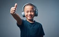 The best beats for a boy like me. Studio shot of a cute little boy using headphones and showing thumbs up against a grey Royalty Free Stock Photo