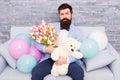 Best boyfriend ever. Romantic man with flowers and teddy bear sit on couch waiting girlfriend. Romantic gift. Macho