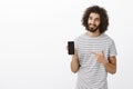 Best choice for modern people. Joyful handsome male model with beard in striped t-shirt, showing smartphone and pointing Royalty Free Stock Photo