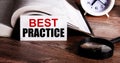 BEST PRACTICE written on a white card near an open book, alarm clock and magnifying glass