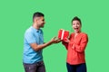 Best present for woman. Young handsome man in casual clothes giving gift box to pleasantly surprised woman. isolated on green