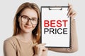 BEST PRICE. Beautiful young business woman wearing glasses holds a clipboard with mock up space isolated on gray background Royalty Free Stock Photo