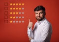 The best rating, evaluation, online rewiew. Happy bearded business showing the hand thumb up in white shirt on red background wi