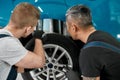 Best service is our duty. Two male mechanics using torch for inspecting wheel of lifted car at auto repair shop Royalty Free Stock Photo