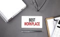 BEST WORKPLACE text written on the card with notebook and clipboard, grey background Royalty Free Stock Photo