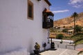 BETANCURIA, FUERTEVENTURA - JUIN 14. 2019: View along facade with wooden old balcony on dry hill and palm tree Royalty Free Stock Photo