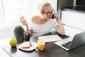 Beuatiful lady working with laptop and talking on smartphone and eating breakfast Royalty Free Stock Photo