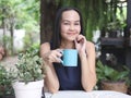 Beutiful Asian woman with long hair sitting in the garden, holding blue cup of coffee, smiling and looking at camera. relaxing Royalty Free Stock Photo