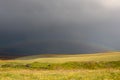 Beutiful rainbow above green meadow after heavy rain with rain clouds and mountains background. Summer season. Fresh green grass. Royalty Free Stock Photo