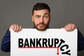 Bewildered businessman holding banner with word BANKRUPTCY and recessing graph, grey background. Collage Royalty Free Stock Photo