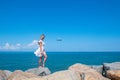 Beyond the Shore: Girl in White Dress, Stones, Sea, and an Airborne Plane Royalty Free Stock Photo