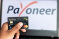 Bhairahawa, Nepal - June 27 2020: Man holds Payoneer Prepaid MasterCard against laptop computer. Payoneer funds were recently put