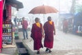 Bhuddist monks in red and yellow holding an umbrella in the foggy people filled streets of dharamshala himachal pradesh