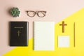 Bible concept with Holy Bible book, notebook, wooden cross and glasses over pink and yellow background. Royalty Free Stock Photo