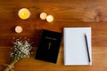 Bible with notebook, candlelight and flower over the wooden background.