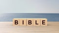 Bible word wooden cubes on table vertical over blur background with sea and sun, mock up, template, Christianity and Catholicism,