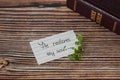 Biblical quote handwritten on lined paper with green plant and a closed holy bible book on wooden background