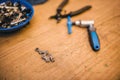 Bicycle chain links lying on a wooden table along with a riveting tool, pliers and spare parts in a blue bowl.
